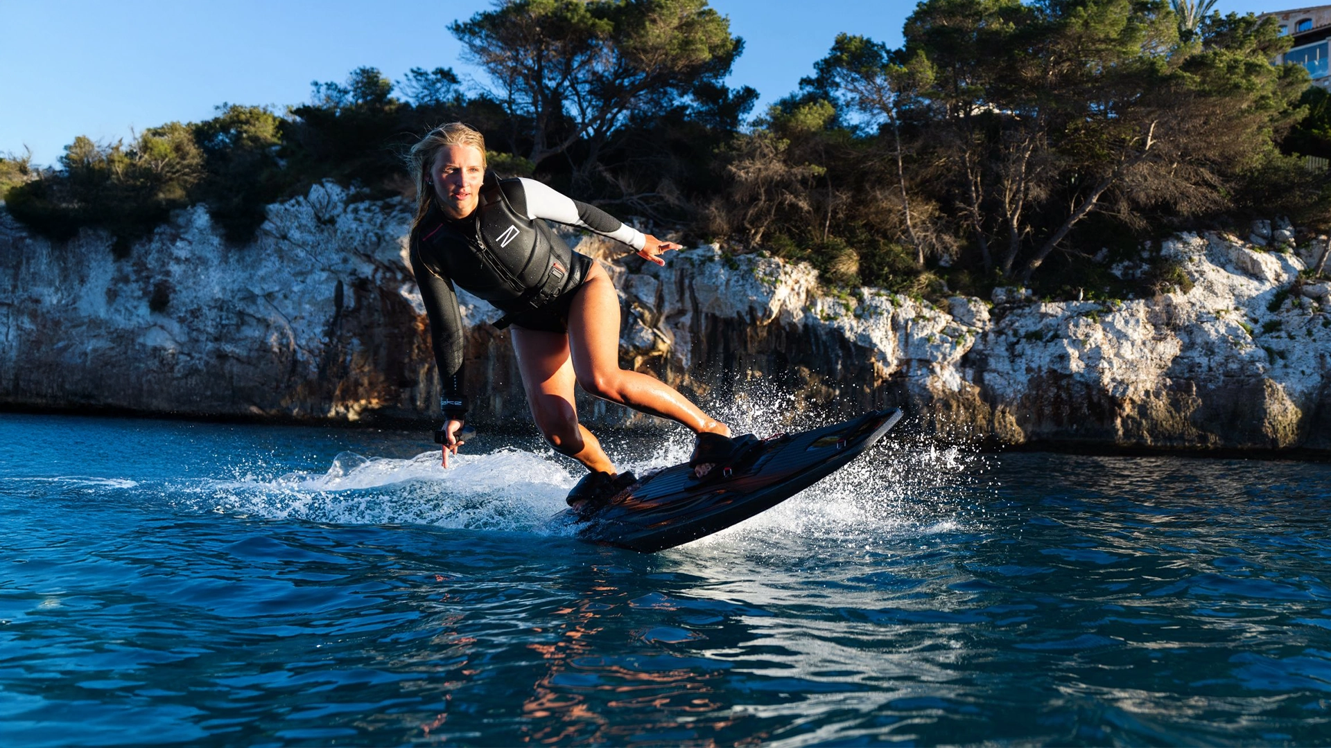 Person Awake boarding on a body of water with rocky cliffs and trees in the background
