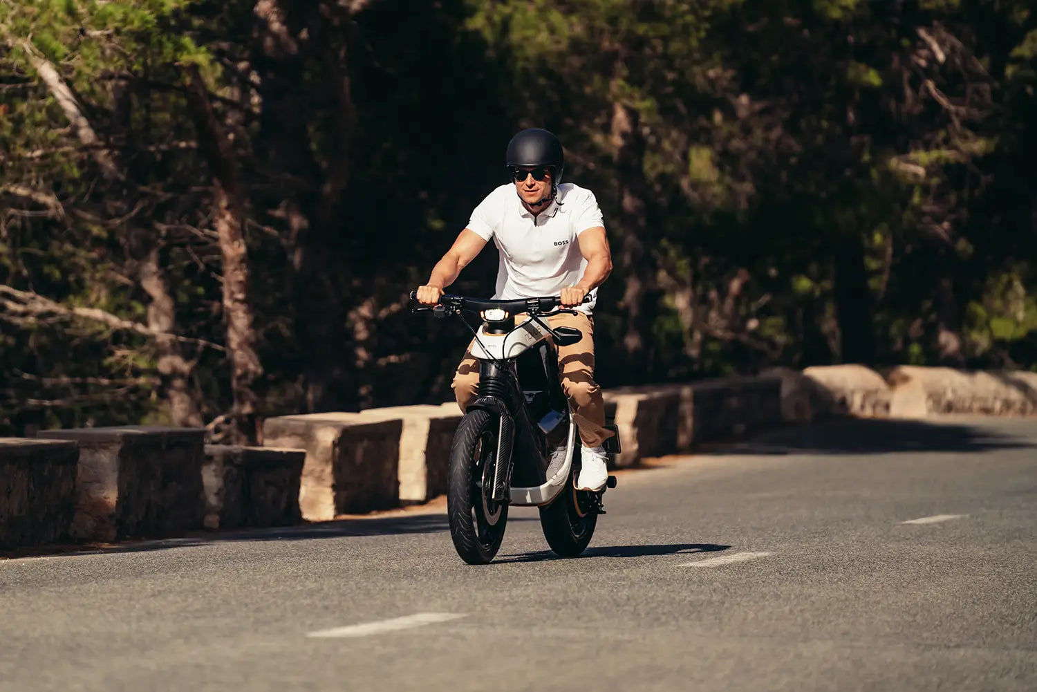 Person riding a NOVUS motorcycle on a road with trees in the background.