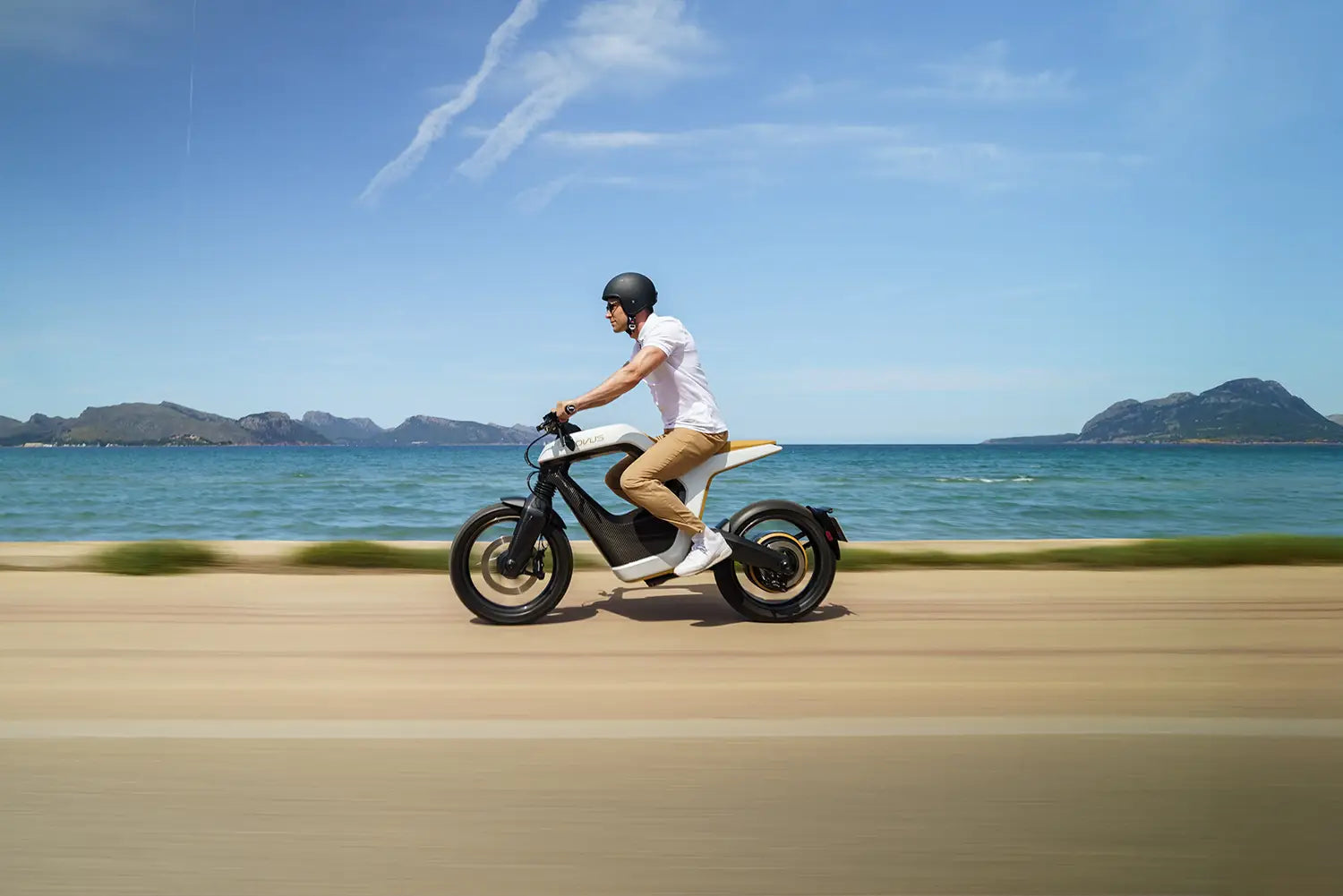 Person riding a NOVUS bike at the beach with mountains in the background.