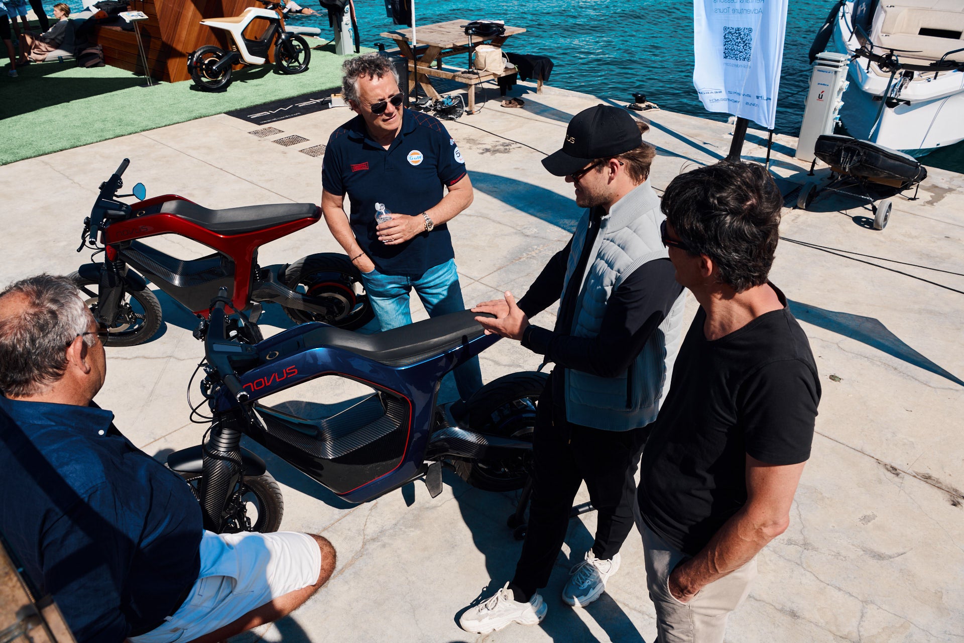 Group of people interacting with NOVUS bikes on a dock by water.