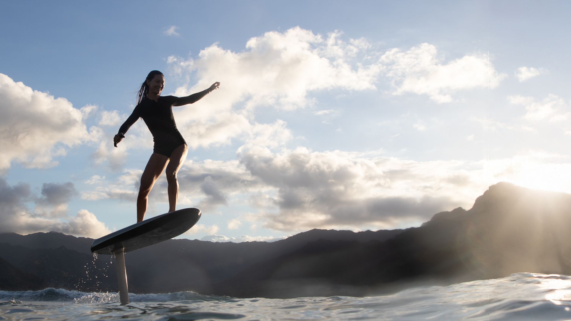 A woman in a wetsuit smiles as she foils on a fliteboard on the sea.