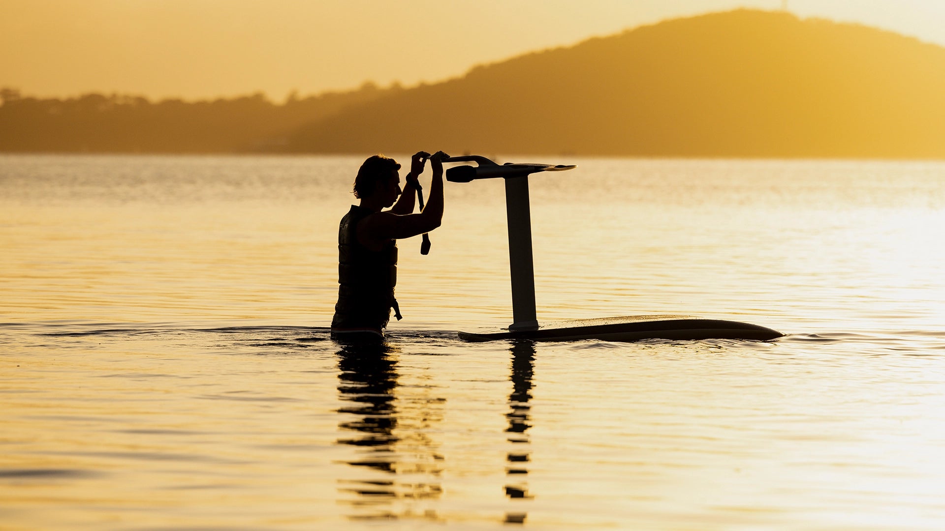 Person holding a fliteboard in the water with a sunset background