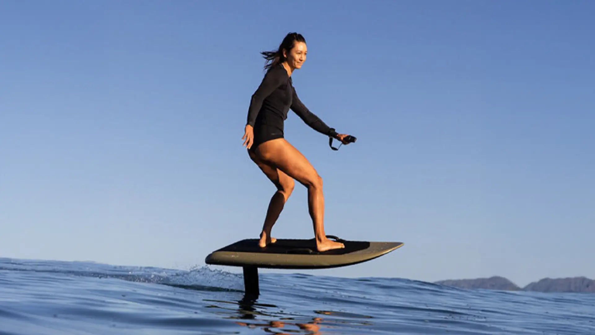 A woman in a short wetsuit flies over the water with her fliteboard and smiles to the front.
