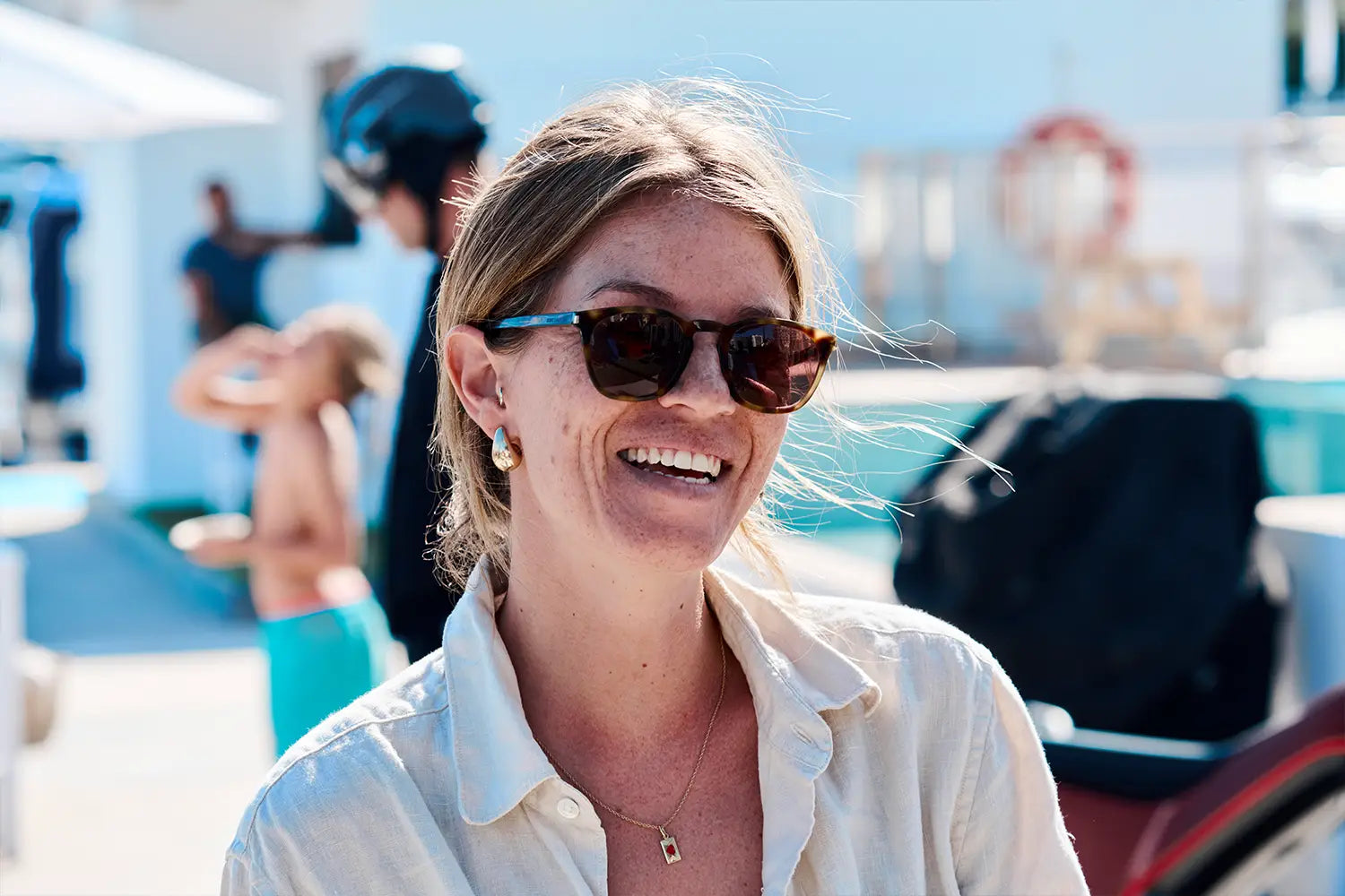 A woman with sunglasses smiles into the camera, in the background you can see a Novus bike and a man in motorbike clothing.
