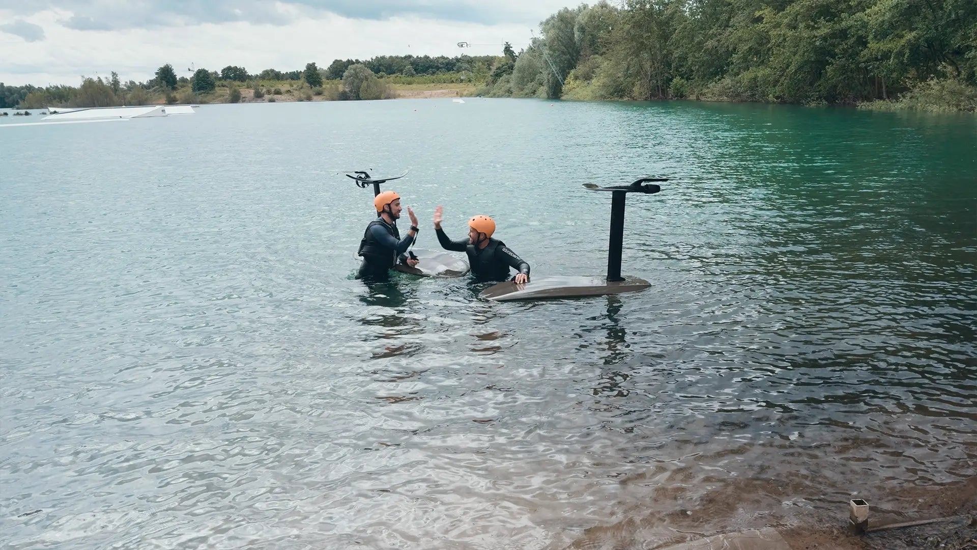 Two people in wetsuits with Fliteboards in the water on a lake.