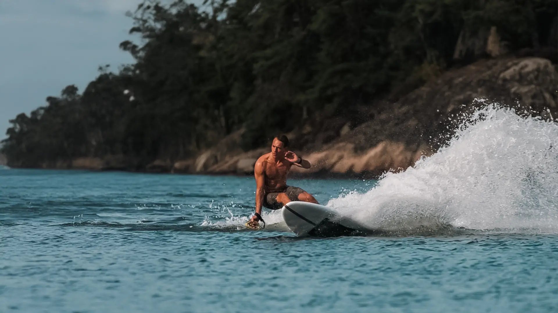 A man in swimming shorts surfs dynamically on the sea with the Lind surfboard.