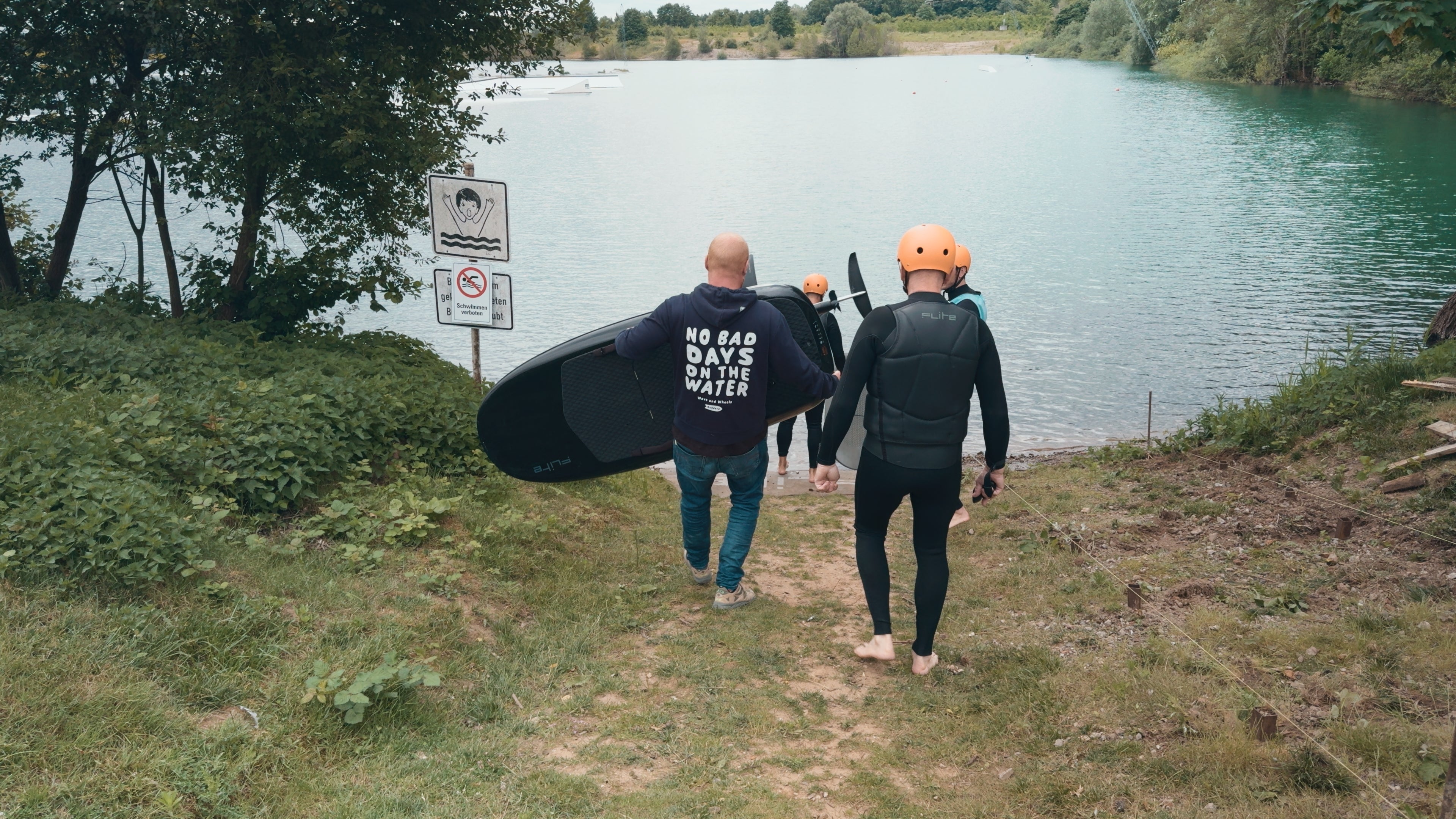 Two people walking along a path by a lake with Fliteboards.