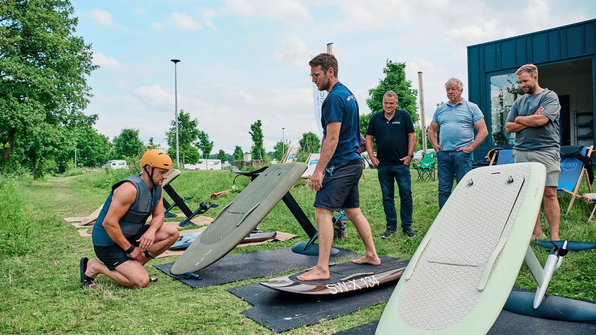 An eFoil instructor is standing on a Fliteboard and explains to a group of people how it works.