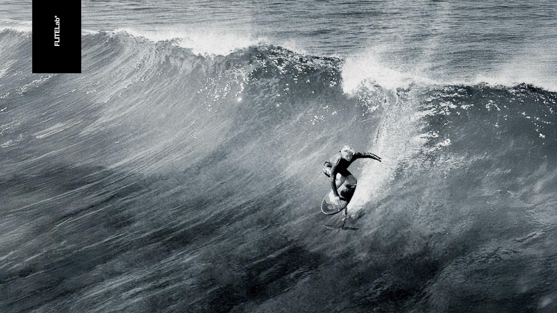 Black and white photo of a surfer riding a wave with FliteLab.