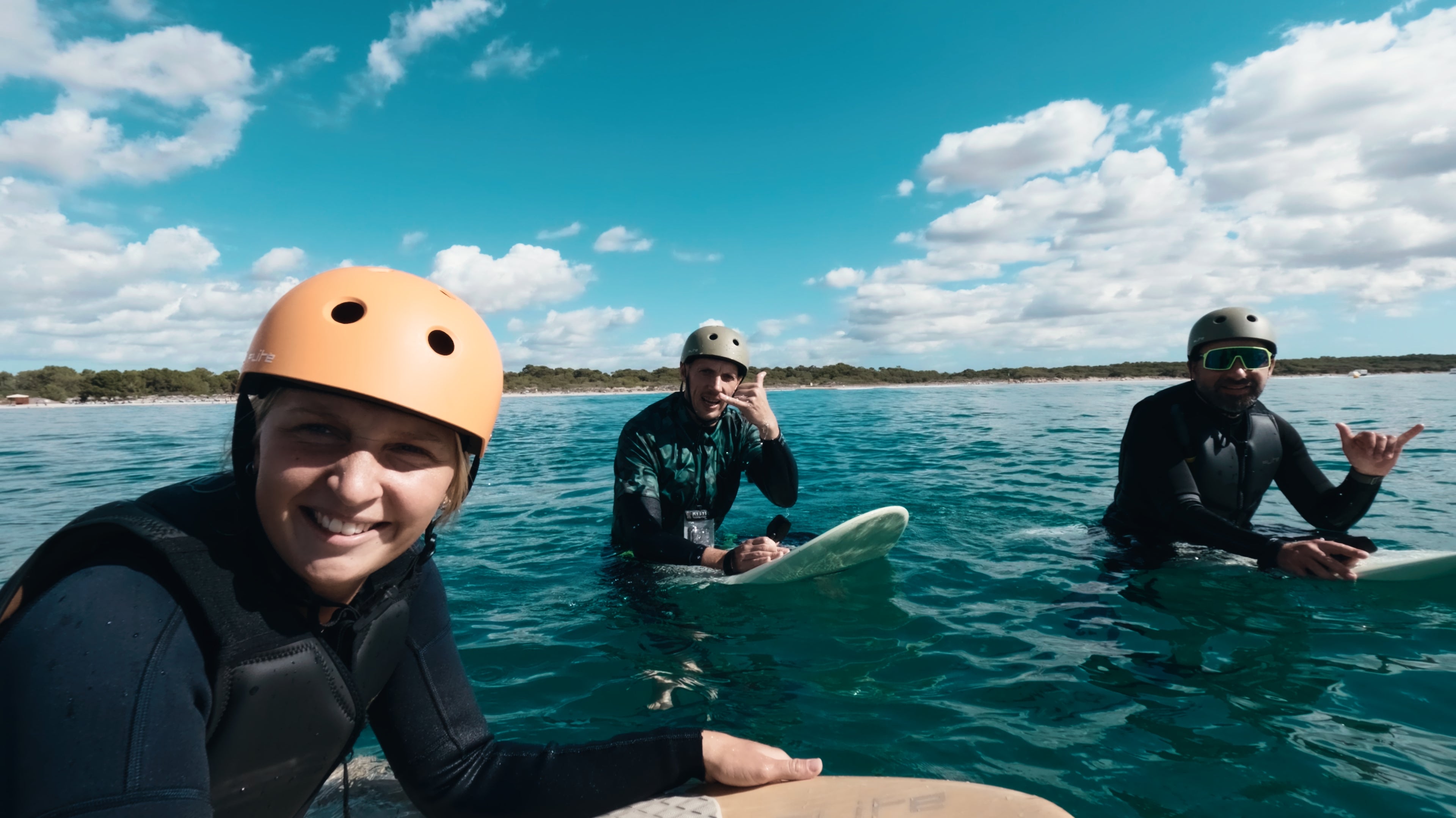 Three people sit on the sea on their Fliteboards in wetsuits and Flite helmets and smile into the camera.