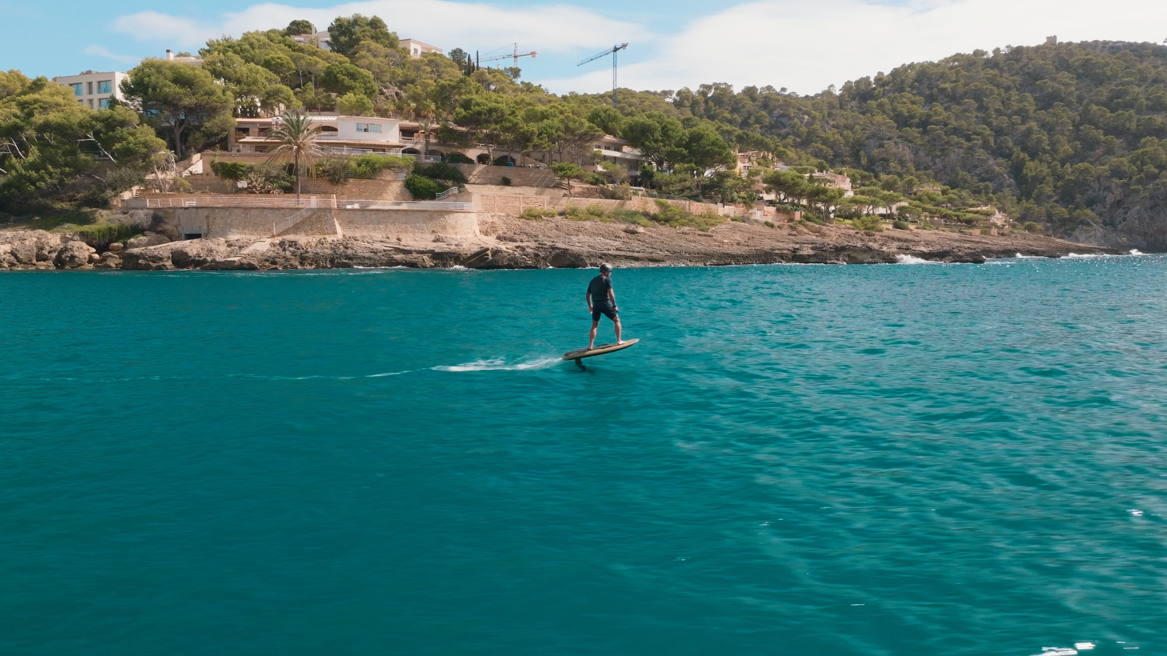 A person efoils on a fliteboard on the sea, with mediterranean mountains in the background.