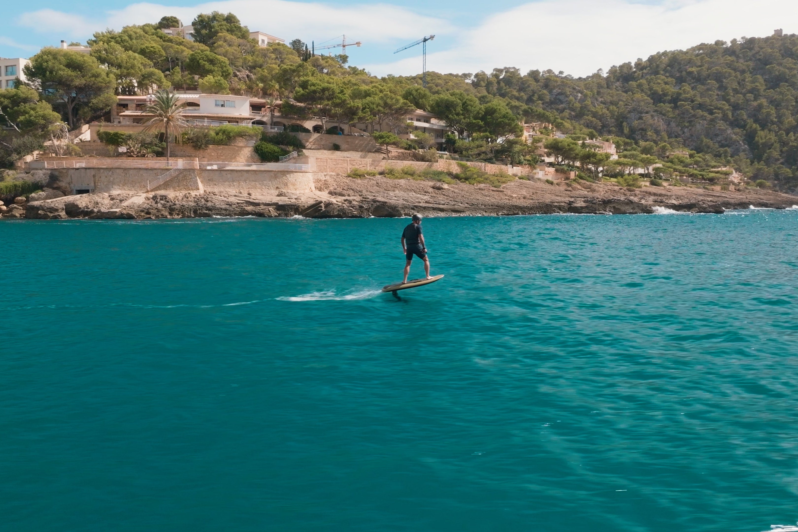 Eine Person efoilt auf einem Fliteboard auf dem Meer, mit mediterranen Bergen im Hintergrund.
