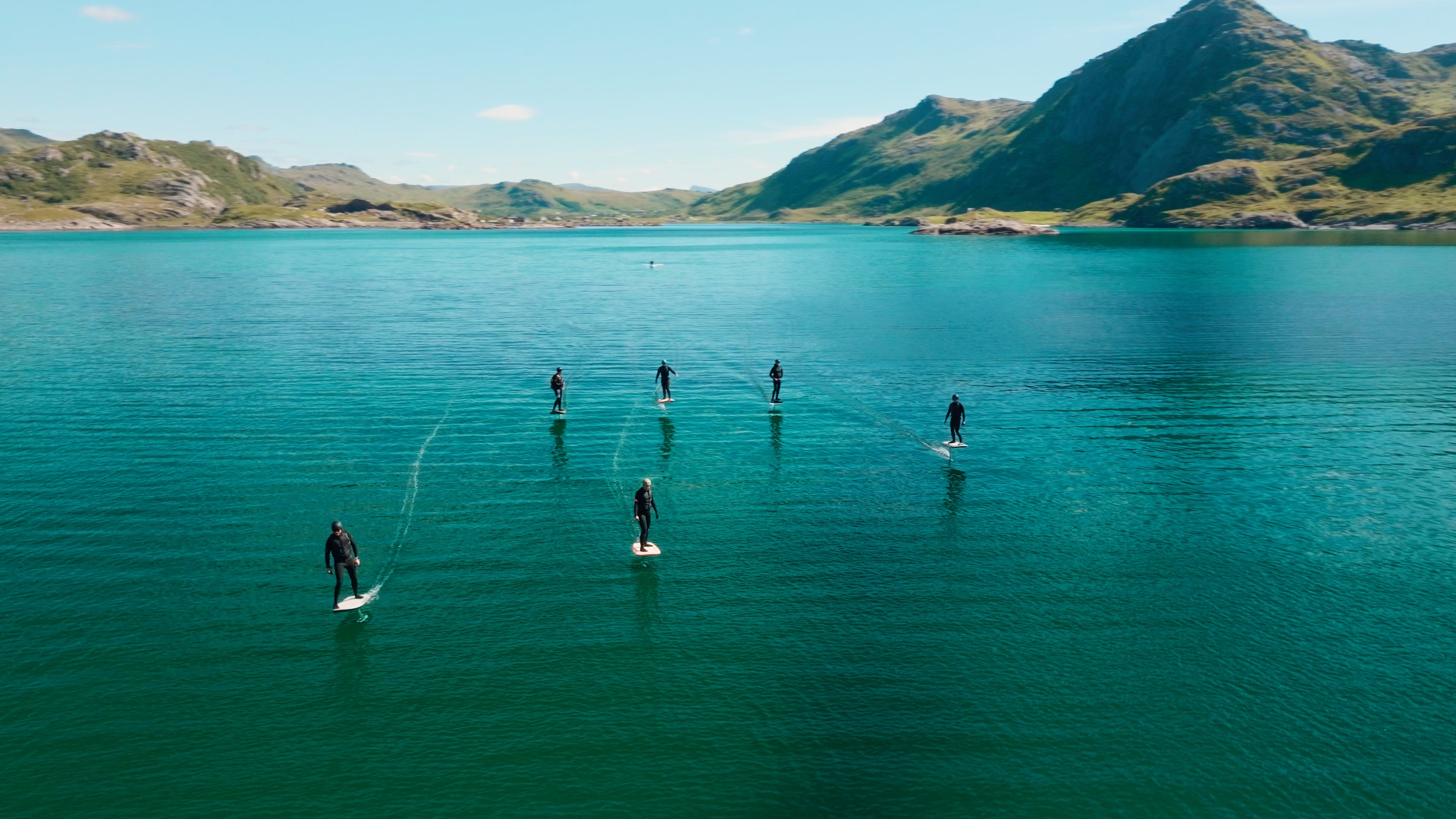 Six people eFoiling on Fliteboards in Norway on the turquoise water, in the background you can see a beautiful landscape with mountains.