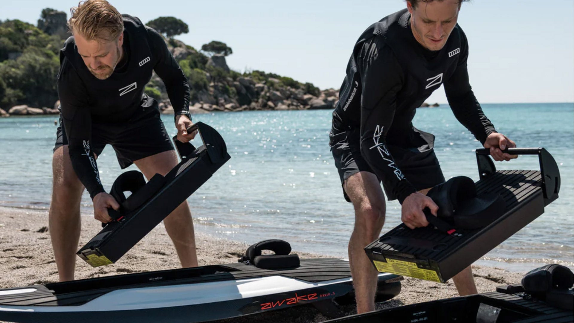 Two male awake instructors standing on a beach and putting batteries into the awake boards.