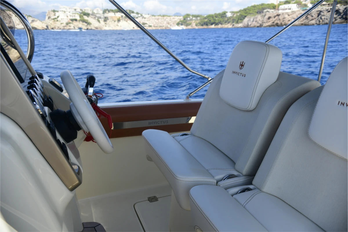 Boat interior with steering wheel and seats, overlooking a body of water.