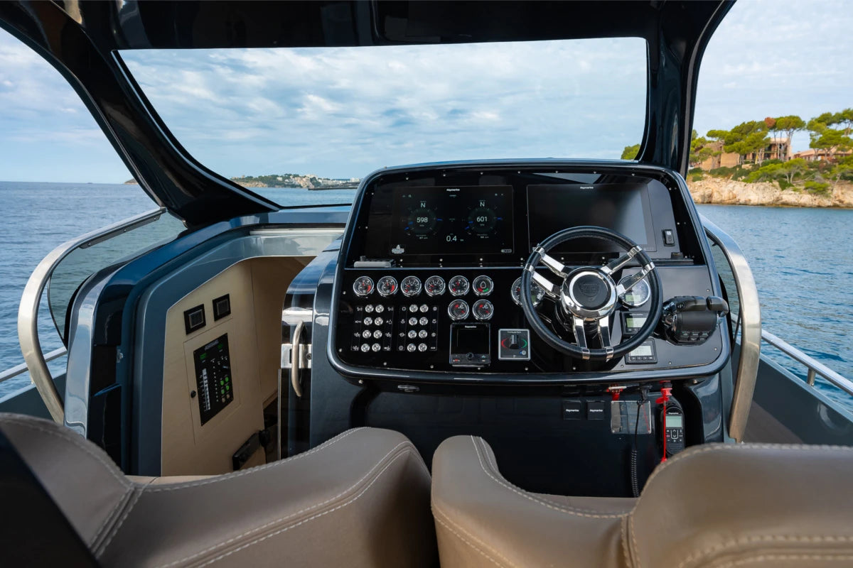 Dashboard of a sinner boat with steering wheel and controls, water and sky visible through windshield.