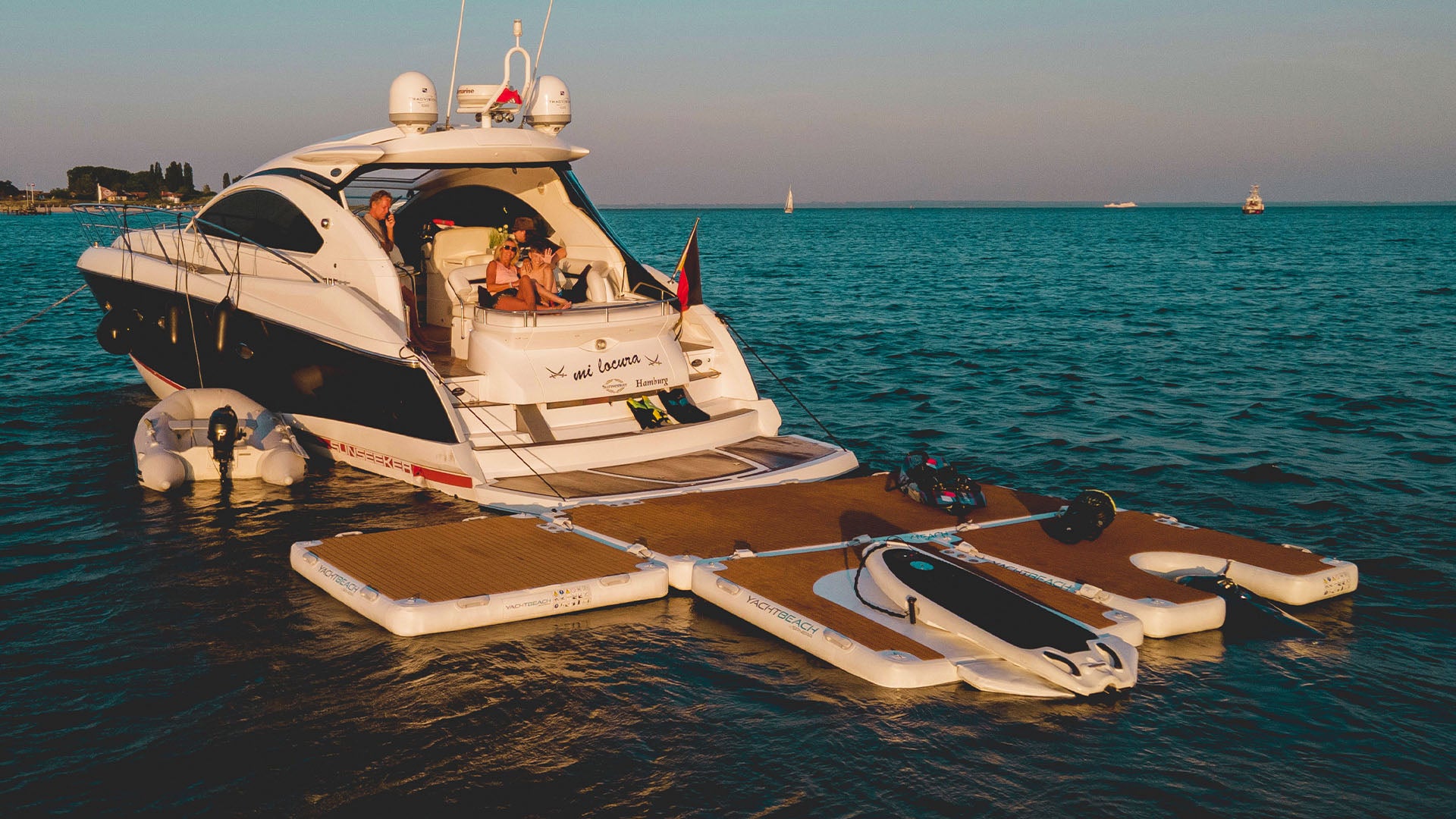 A boat on the water has several floating platforms attached to the back, including a Yacht Beach Foil Dock with an eFoil secured to it.