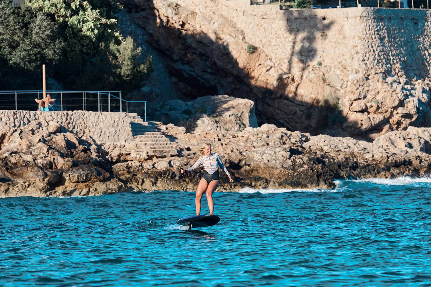 Eine Frau fährt mit einem blauen eFoil  Fliteboard dem Meer vor Mallorca.