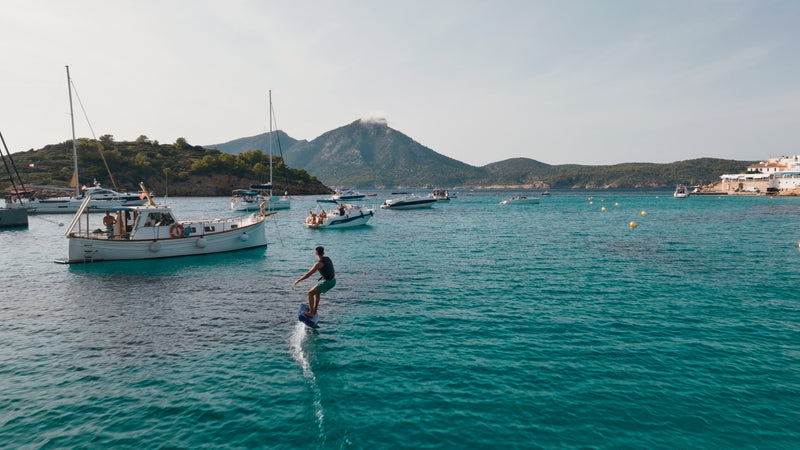 A person efoils on his fliteboard on the sea between boats.