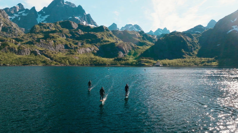 In the middle of Norway, 5 people are foiling on a fliteboard on the water, with mighty mountains in the background.